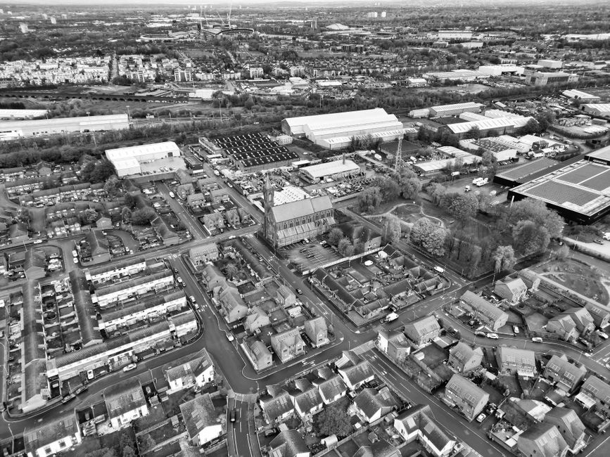 Aerial black-and-white photograph of a suburban area showing a variety of residential houses with pitched roofs, narrow streets, and small gardens. In the center, there is a tall brick building with a